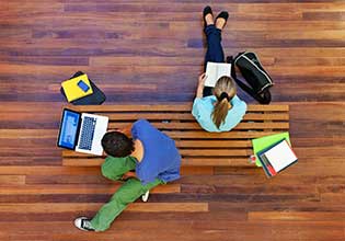 two students sitting on the floor and using their laptops 