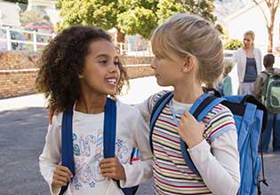 two girl smiling at each other and wearing backpacks
